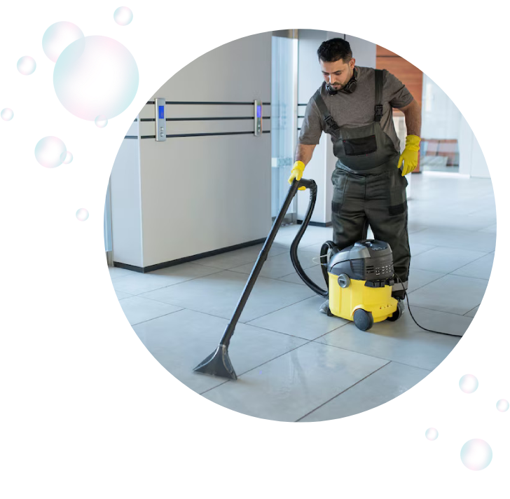 A man in grey overalls is vacuuming the floor.